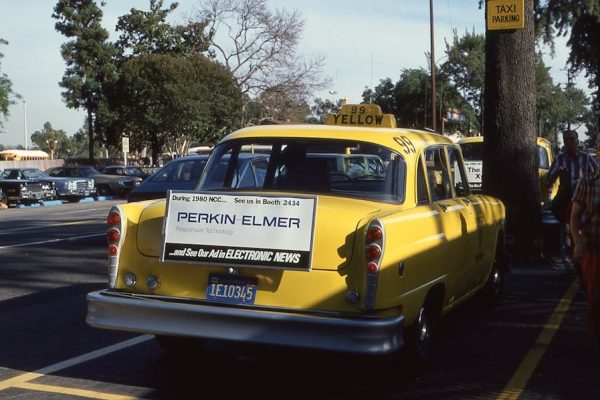 A vintage yellow taxi with an advertisement, parked on an urban street.