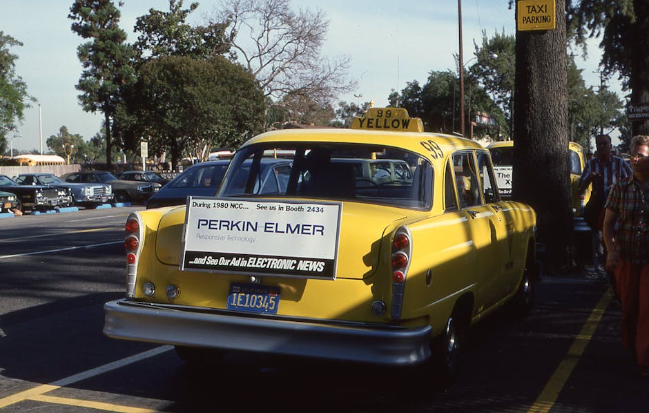 A vintage yellow taxi with an advertisement, parked on an urban street.