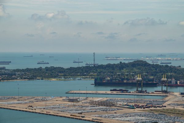 Aerial perspective of Singapore's bustling harbor with ships and shipping containers under a clear sky.