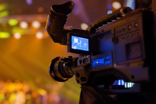 Detailed view of a video camera capturing a live event on stage with blurred lights in the background.