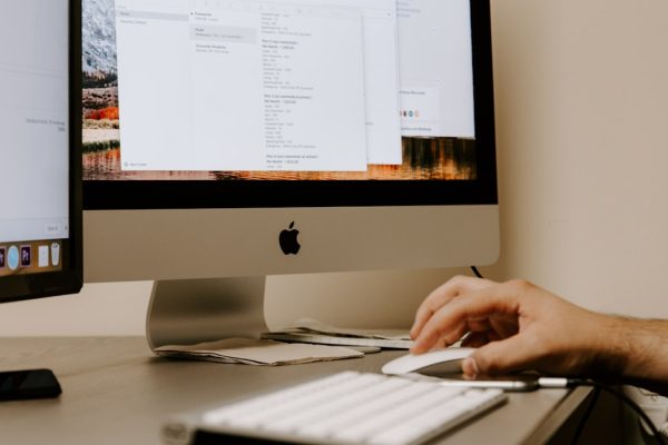 person holding white Apple Magic Mouse beside iMac and keyboard
