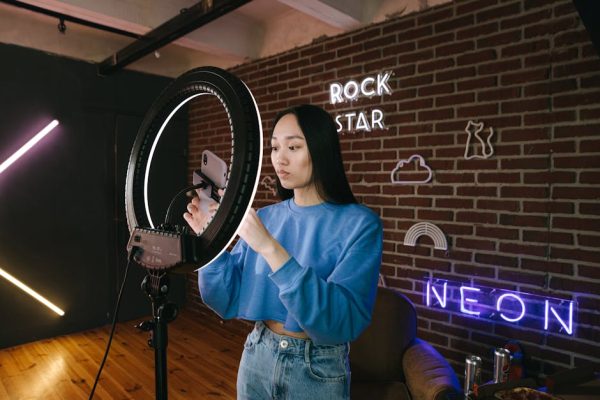 Asian woman influencer sets up a ring light in a neon-lit room for content creation.