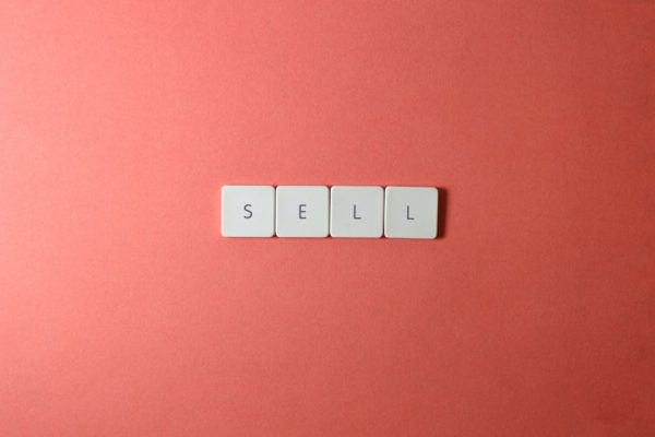 Close-up of keyboard tiles spelling 'sell' on a red background, minimalist design.