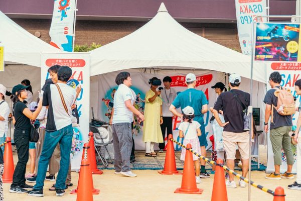 People gather at an outdoor fair booth, enjoying a virtual reality experience in a festive setting.