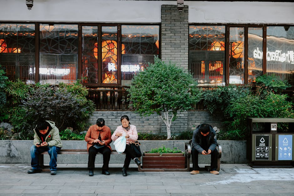 People sitting on a bench in Nanjing, China, using mobile phones, showcasing urban life.